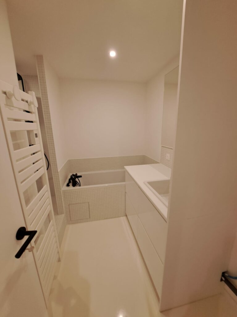 Salle de bain moderne blanche avec baignoire, douche et meuble vasque après rénovation au Touquet-Paris-Plage